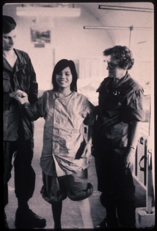 Young Vietnamese woman with one leg walking with the help of two American medical personnel.