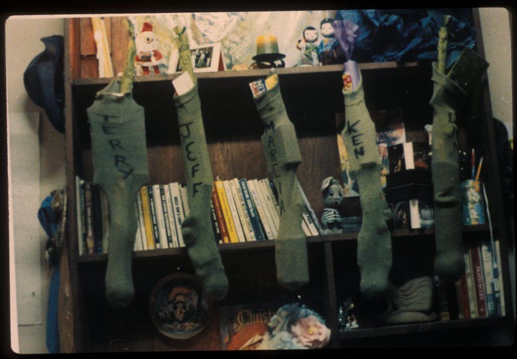 Army green socks stuffed as Christmas stockings, hanging on a bookshelf. Names on socks are written in black marker: Terry, Jeff, Marcia, Ken, Dan.