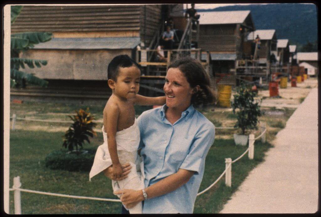 Young U.S. nurse holding a young Asian child outside of hospital.