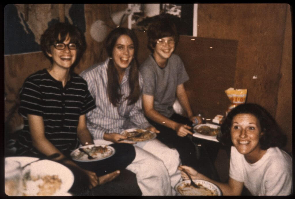 Four young U.S. nurses smile for the camera while eating a meal together.