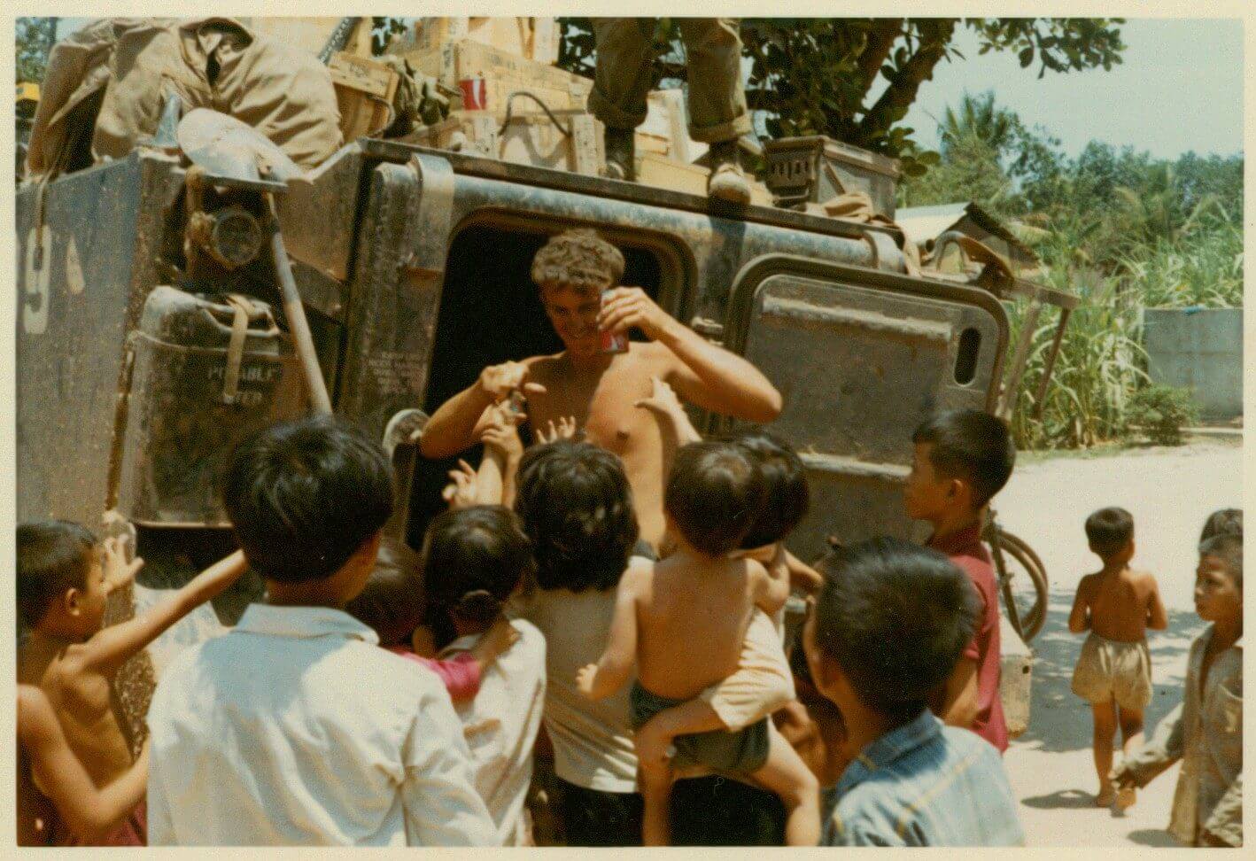 A young G.I. holding a Coke, Vietnamese children reaching up all around him.