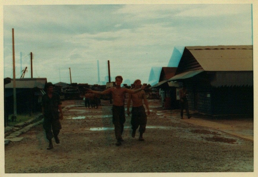 Young U.S. soldiers walking through a village, shirtless.