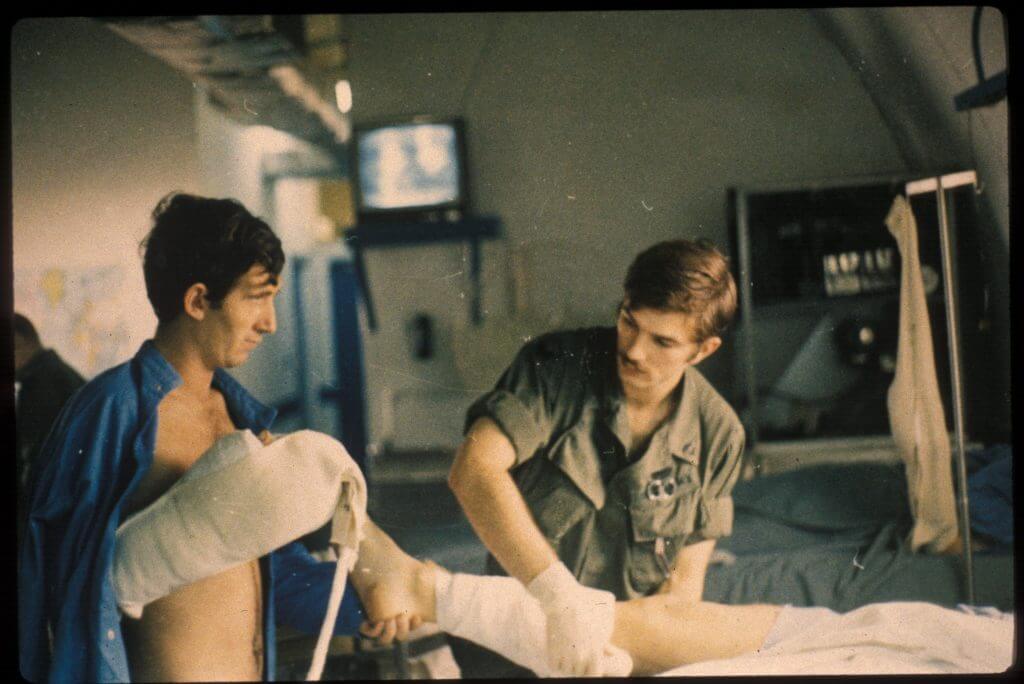 A U.S. corpsman bandages up the leg of a patient with the help of another patient.