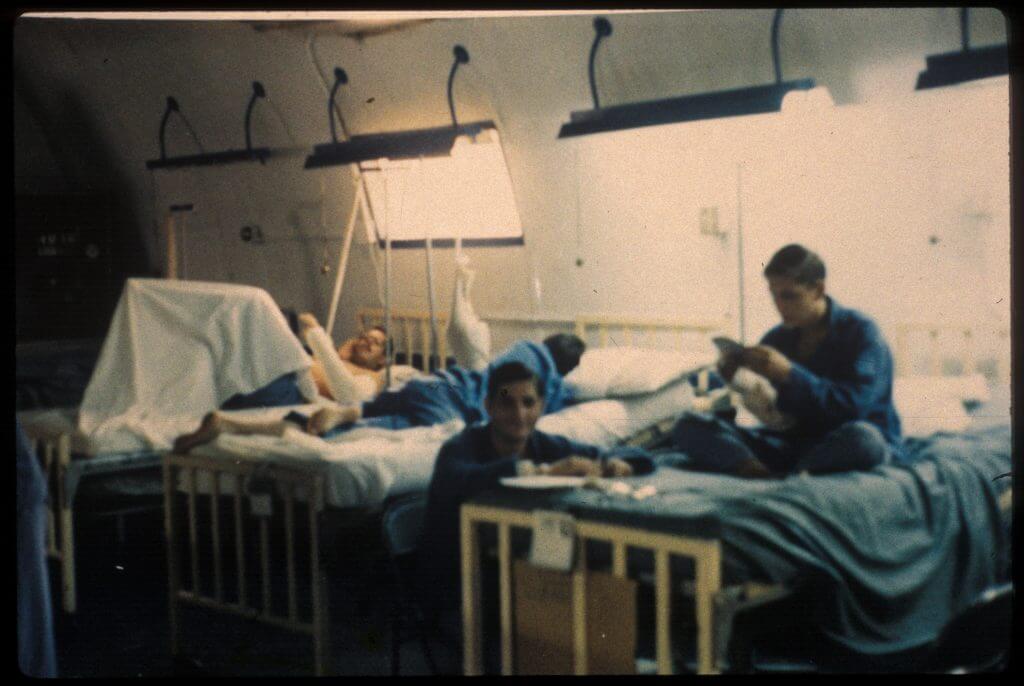 Color image of 4 patients in blue pajamas recuperating in the hospital ward.