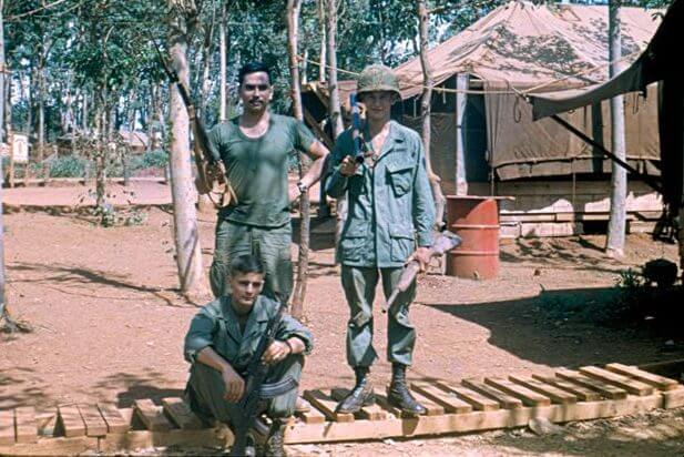 Three soldiers standing with their rifles outside a camp.