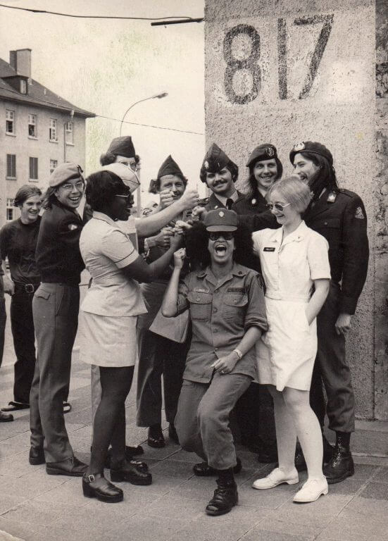 Group of soldiers and nurses posing happily for a photo with their fists all held towards the center.