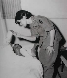 Young nurse standing over a patient's bed, his hand in hers.