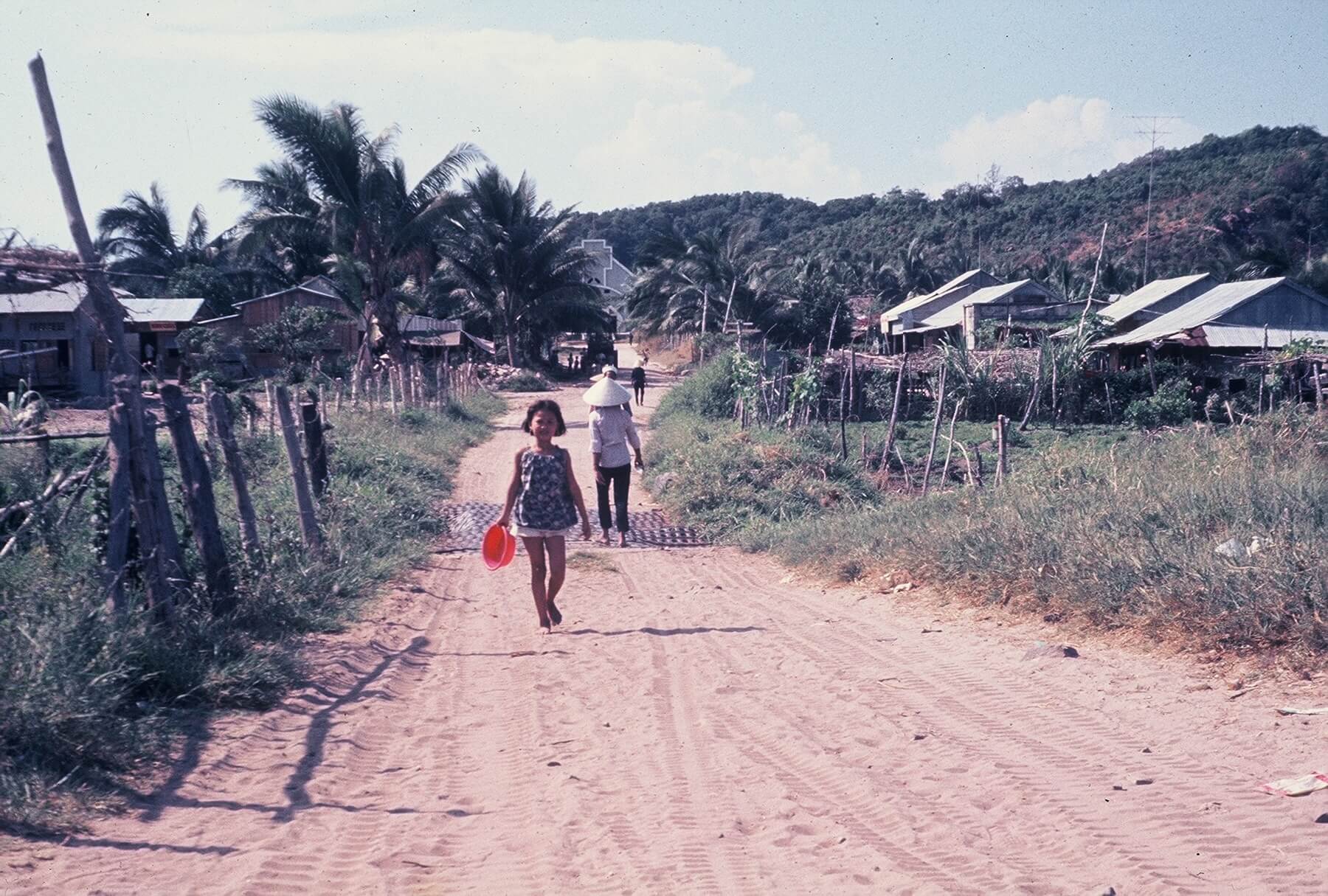 Vietnamese civilians in a village, young girl walking towards the camera.