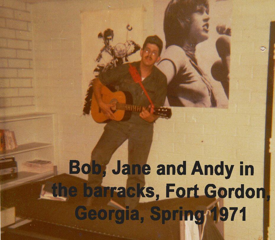 Young soldier standing on barrack bunk, strumming guitar, in front of Bob Dylan and Jane Fonda posters.