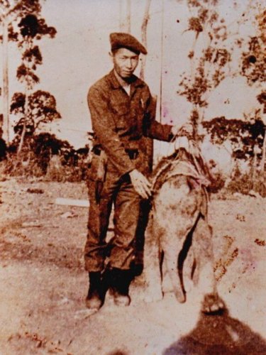 Sepia toned photo of young Asian soldier in uniform, posing with a baby elephant.