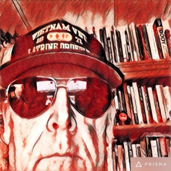Red and white stylized photo of Tim wearing a Vietnam vet ball cap and aviator sunglasses.
