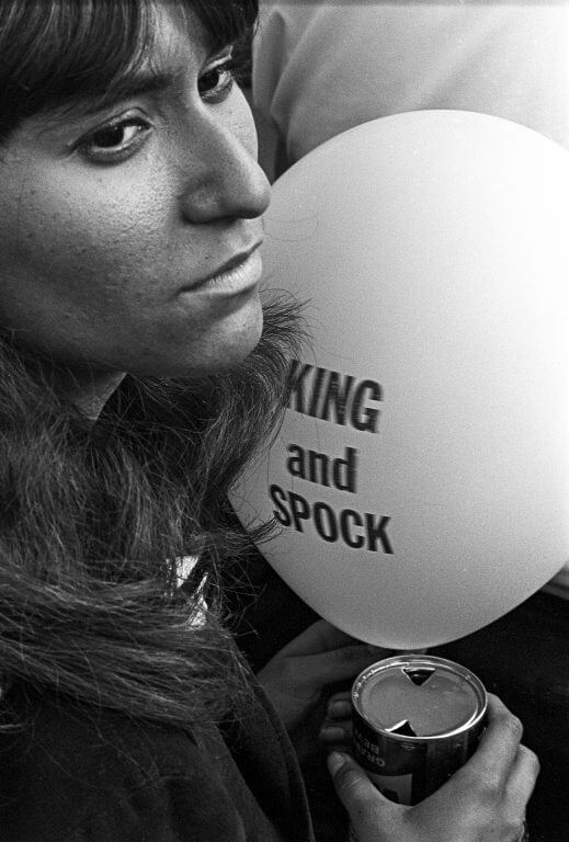 Young female protester holding a canned beverage and a white balloon that says "KING and SPOCK."