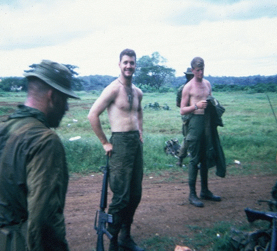 Two shirtless young soldiers, standing outside.