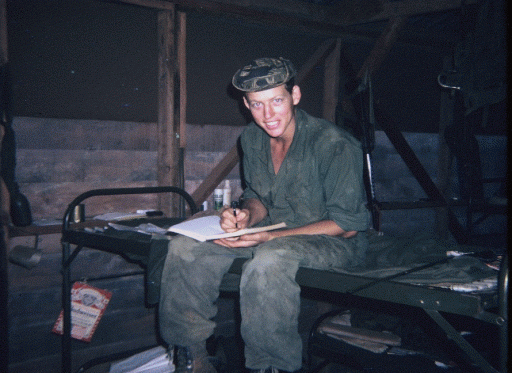 Young soldier sitting on a cot writing in a notebook.