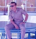 Young soldier sitting on a table outside.