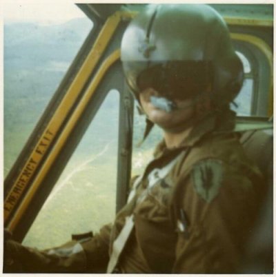 Helicopter pilot with helmet and sun visor, posing for a picture while flying.