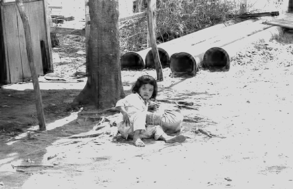 Asian child sitting on the ground outside with a frightened look.