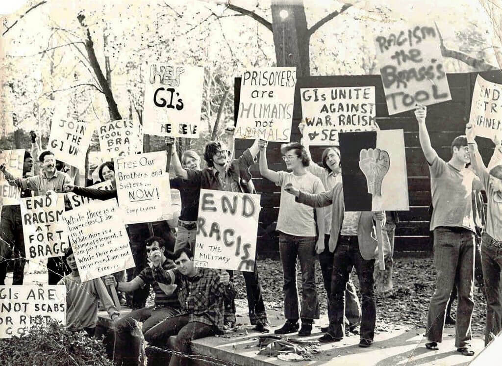Group of about a dozen American soldiers protesting on the streets, holding signs.