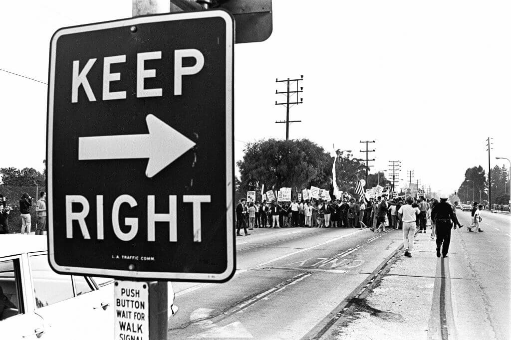 A street sign that reads "Keep Right" with a crowd of people off in the background.