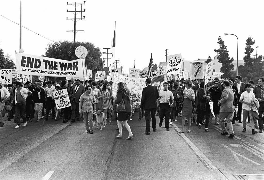 Protesters walking toward the camera with signs that read things like "Stop War" and "End The War".