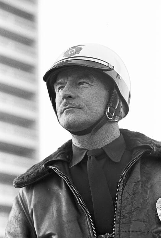 Close up of a middle-aged man wearing a bomber jacket and a helmet.