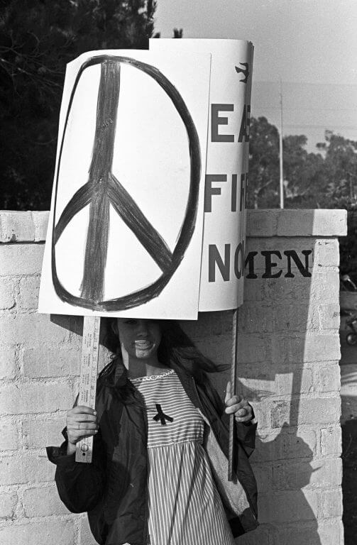 Young female protester holding up a sign with a peace sign on it.