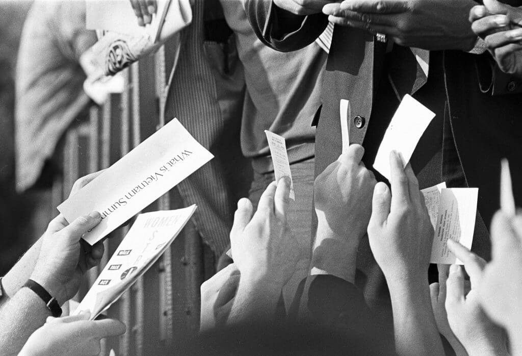 Protesters from the crowd handing their draft cards and other slips of paper up to he signed by Muhammad Ali.