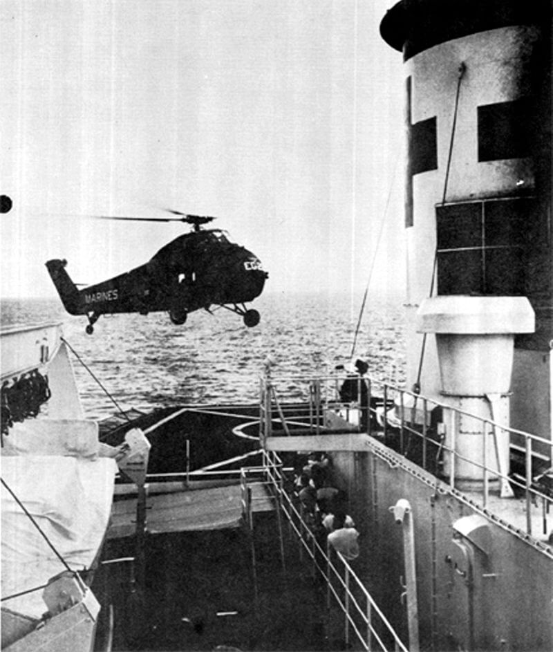 A chopper approaching the landing pad of a large ship.