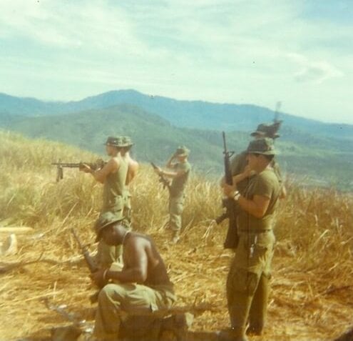 Group of U.S. soldiers with rifles, mountains in the background.