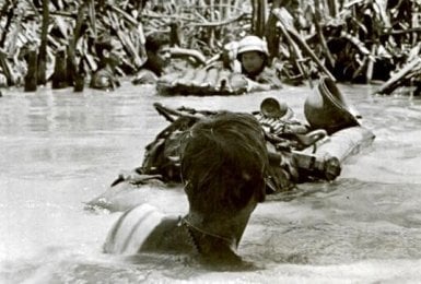 Soldiers neck-deep in water, crossing a canal.