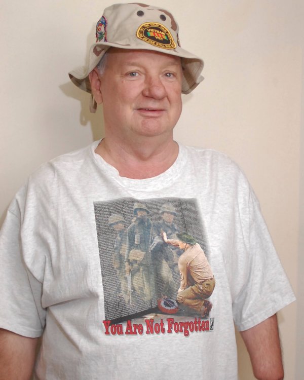 Contemporary photo of an aged U.S. veteran with one arm, smiling, in a boonie hat with a Vietnam memorial t-shirt.