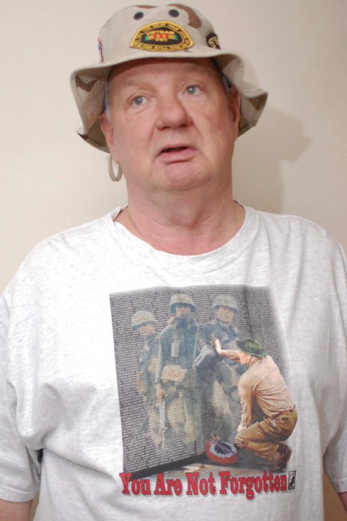 Contemporary photo of an aged U.S. veteran with one arm, looking confused, in a boonie hat with a Vietnam memorial t-shirt.