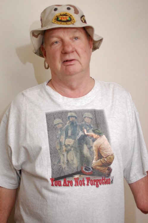 Contemporary photo of an aged U.S. veteran with one arm, looking tired, in a boonie hat with a Vietnam memorial t-shirt.
