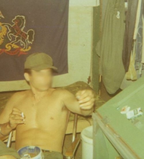 Photo of a shirtless soldier with a cigarette in his hand, reaching toward the pack. Face is blurred out.
