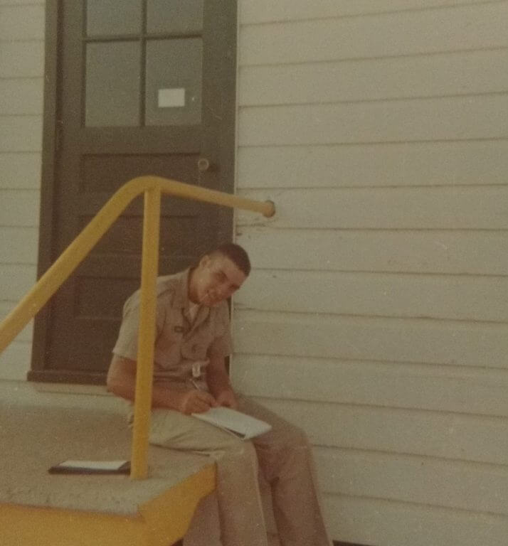Young soldier sitting on stoop outside a building, writing on a pad of paper.