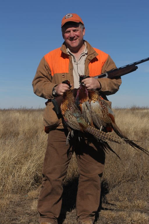 Contemporary photo of a man in hunting gear, holding a rifle and some pheasants.