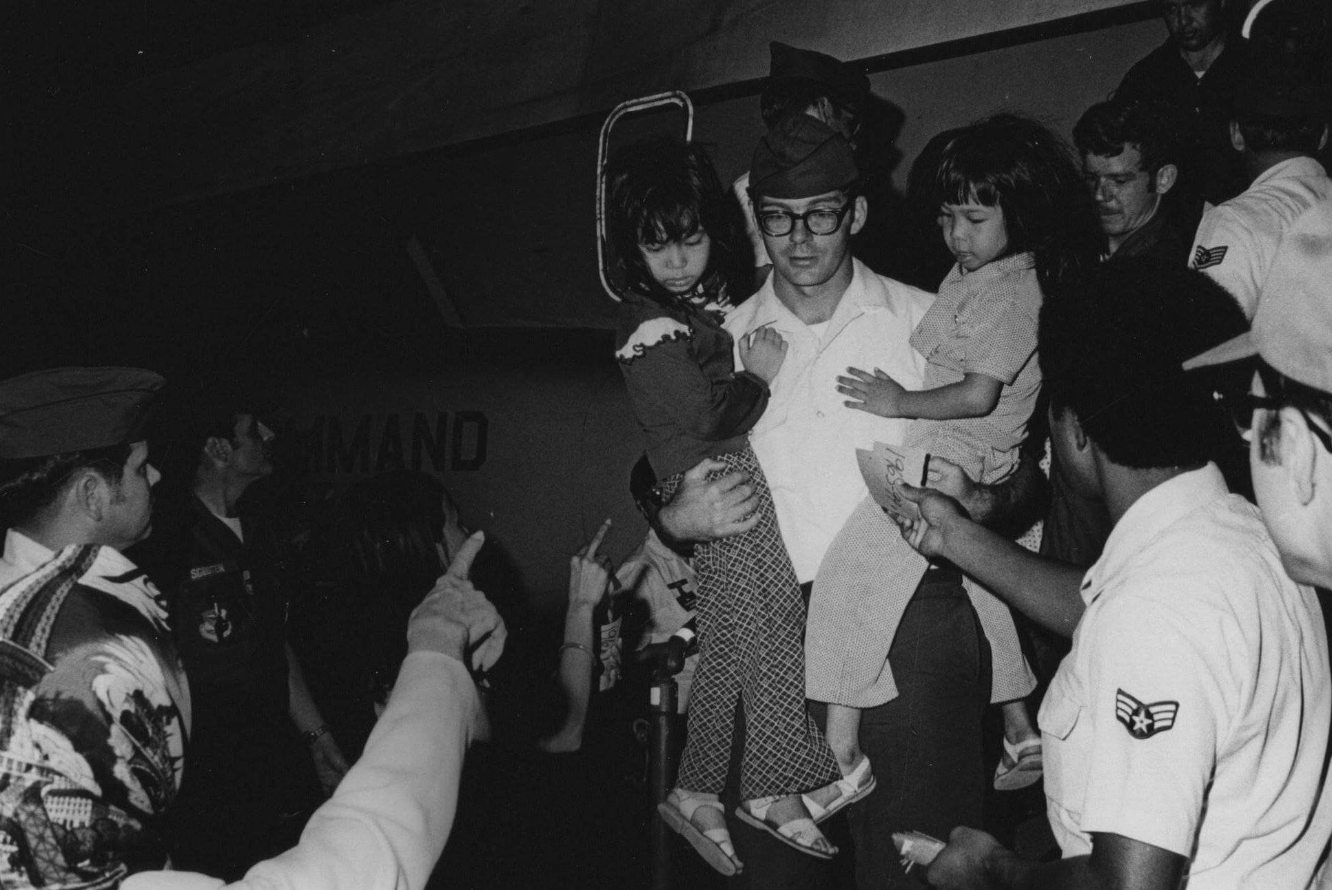 American soldier carrying two small Asian children, deplaning.