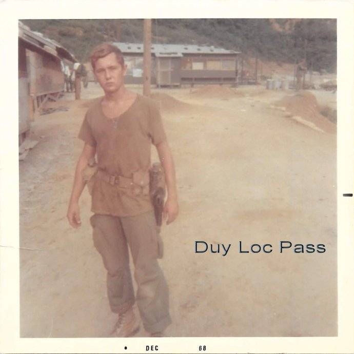 A young soldier standing in a dirt clearing. Text says: "Duy Loc Pass."