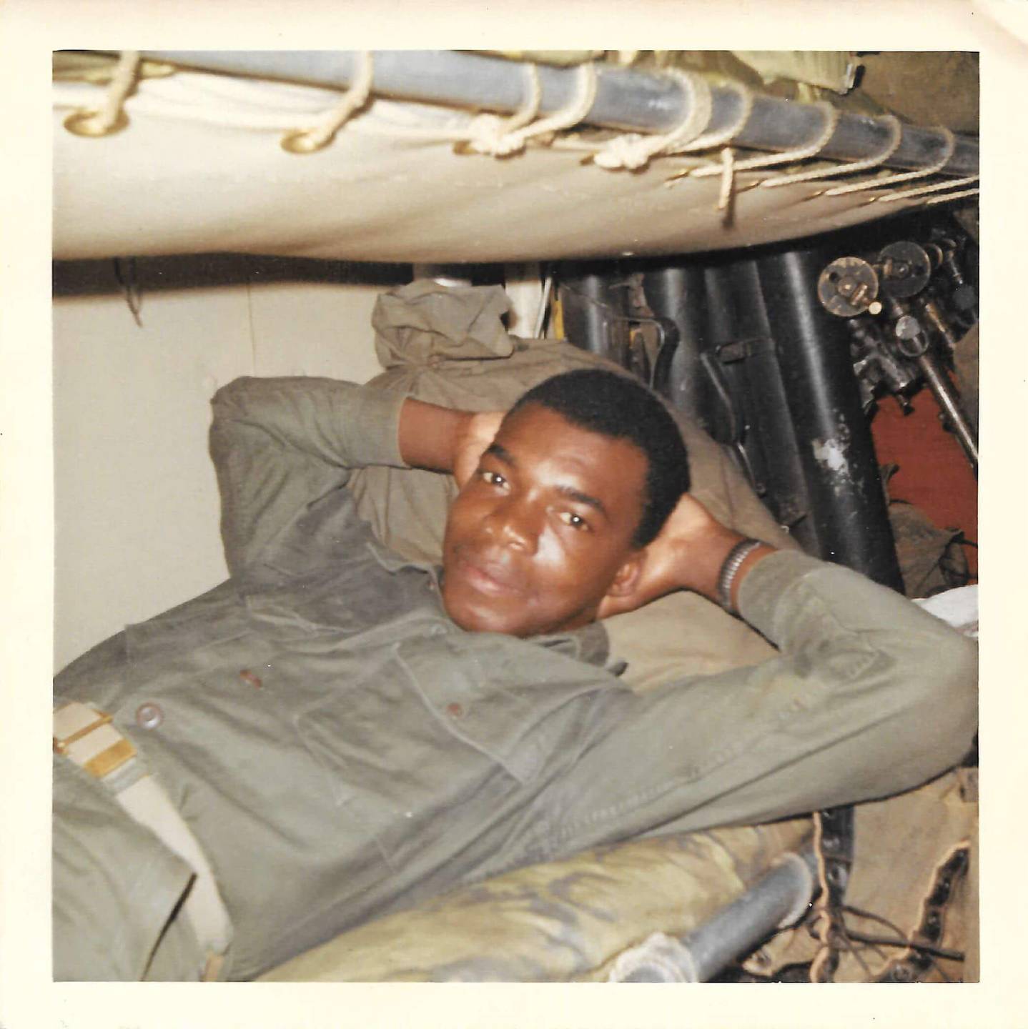 A young soldier relaxes on his back in his barrack bunk, hands behind his head.
