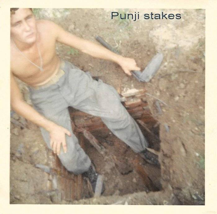 Young shirtless soldier sitting in a hole in the ground. Text reads: "Punji stakes."