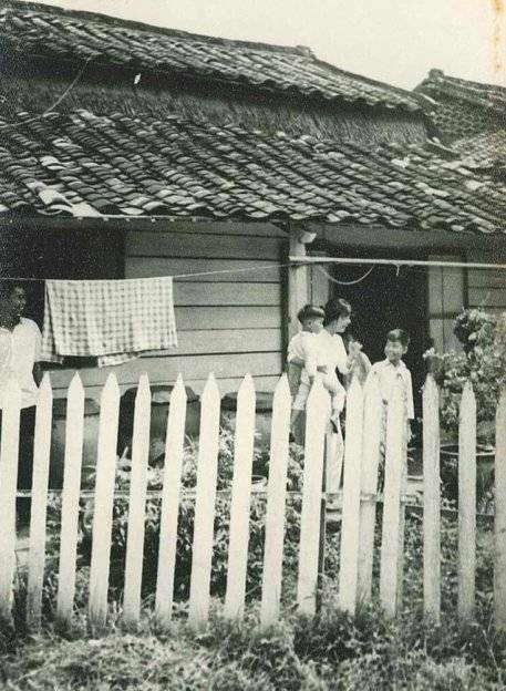 An Asian residence with white picket fence, mother and children smiling within.