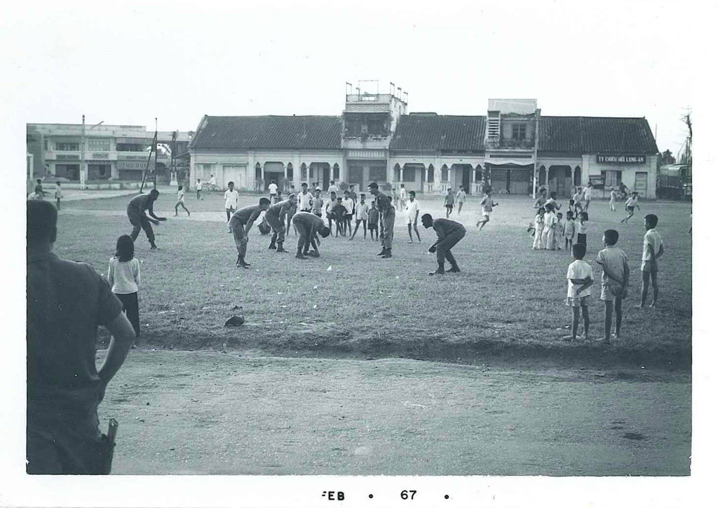 U.S. soldiers playing football while a crowd of Asian children observe. Photo dated Feb 67.