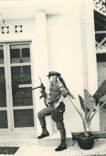 A soldier with his gun propped on his knee, standing guard outside a building.