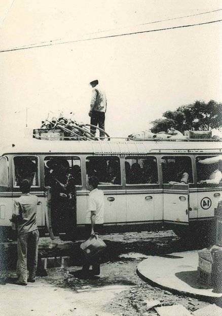 Asian men loading up cargo on top of a bus.