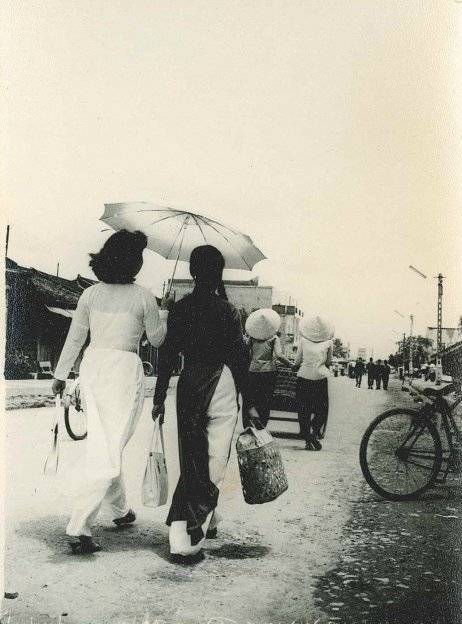 Asian woman walking under a parasol along a city street.