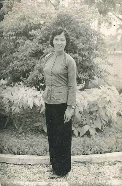 A young Asian woman posing for a photo in a garden.