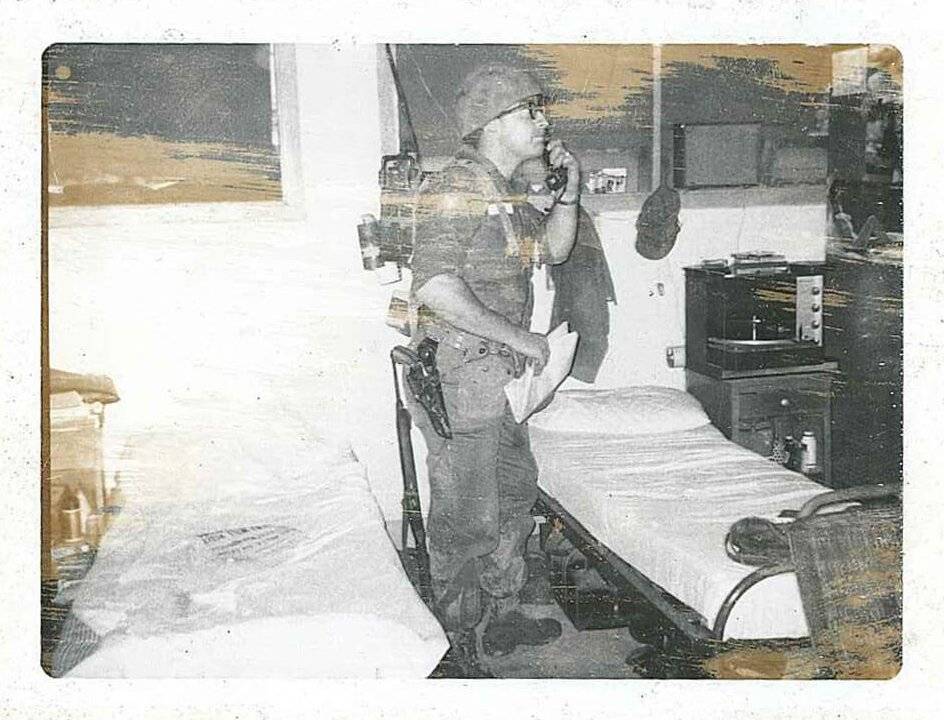 A U.S. soldier in full gear standing in a barracks and talking on the telephone.