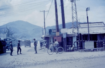 A village with people on the dirt road, mountain rising up in the background.