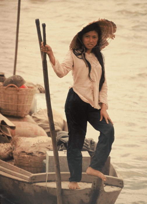 Young Vietnamese woman with a straw hat, standing on a fishing boat.