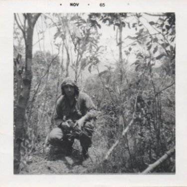 A young U.S. soldier crouched down in jungle. Photo is dated Nov 65.